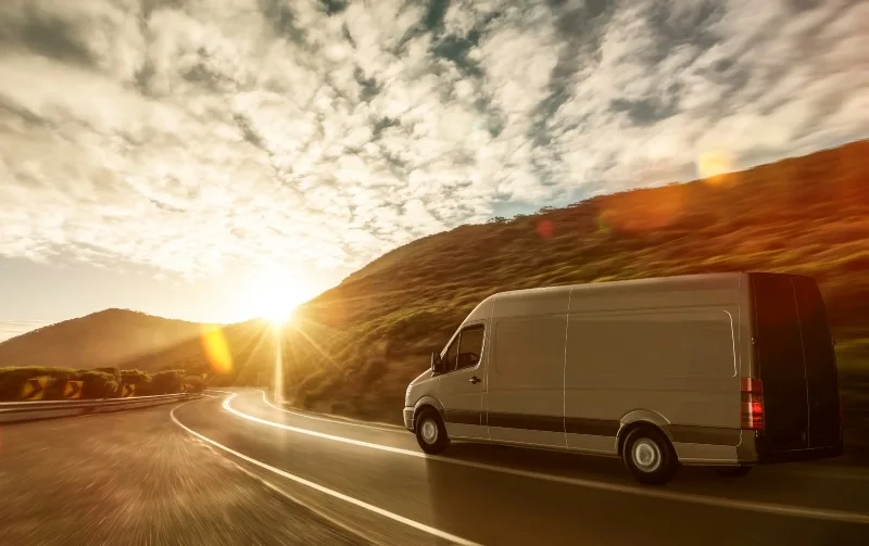 White delivery van driving with low sun