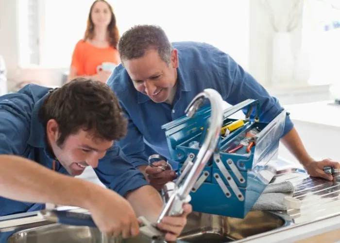 Plumbers in overalls repairing a broken sink