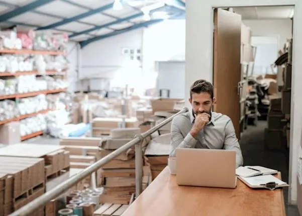 A man is looking at his laptop in a warehouse