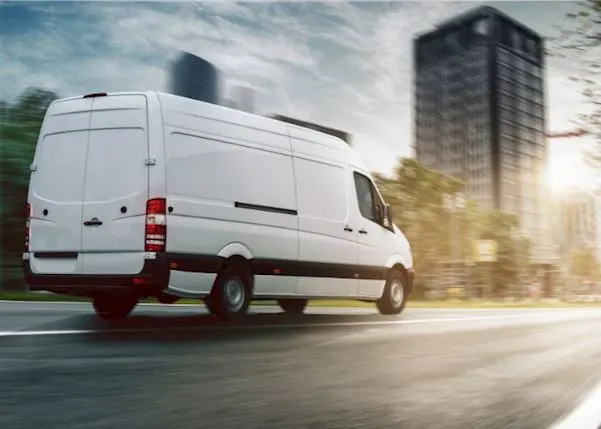 White van driving towards a city