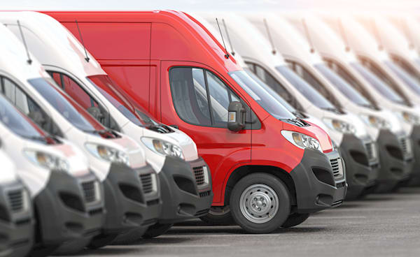 a row of vans with a red one standing out in front of a row of white vans.