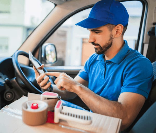 Delivery driver dressed in blue is sat in his van looking at the delivery driver management software