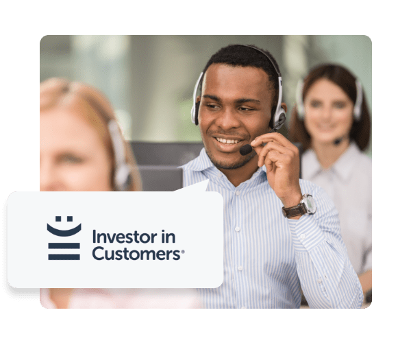Man with headset on is sat at his desk in between two women with headsets on. In the bottom left there is a speech bubble coming from the man with the Investors in Customers logo.