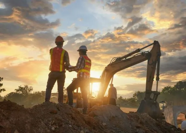Two construction workers in hardhats and high visibility looking over the project plans