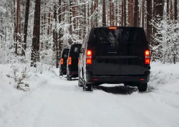 Row of black vans driving in a row on a snowy road