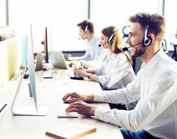 2 men and 1 woman with headsets on, the closest man is speaking with a customer about their truck tracking system