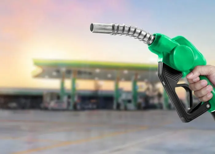 Person holding a fuel pump with a petrol station in the background