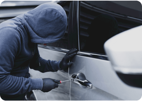 Man in a dark blue hoodie breaking into a grey car