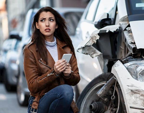 a woman in a brown jacket on her phone after getting in a car accident