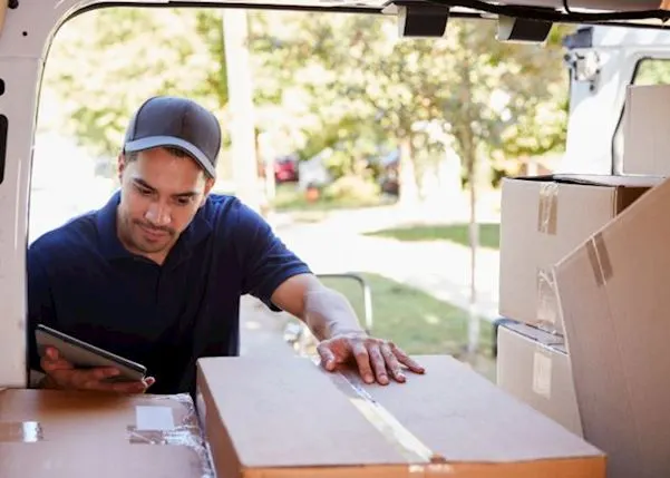 Delivery driver looking at a tablet whilst checking parcels in a vehicle