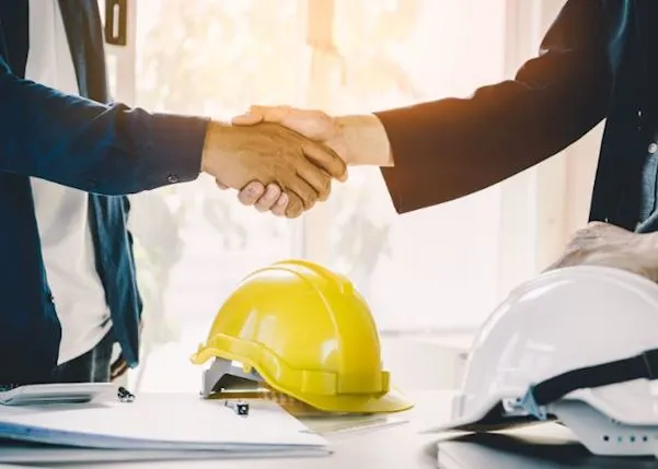 People shaking hands over two hard hats