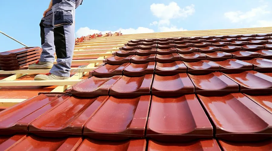 Roofer attaching red tiles to a slanted roof